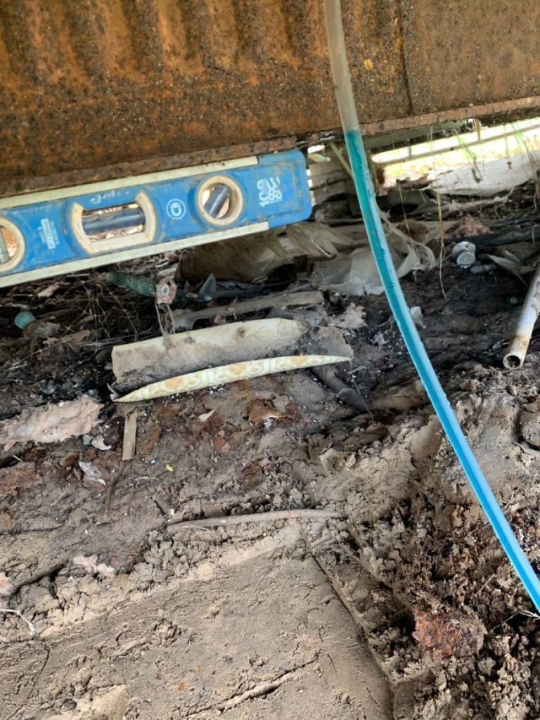 Leveling tool placed under a home to measure and adjust foundation alignment during repairs in East Texas.