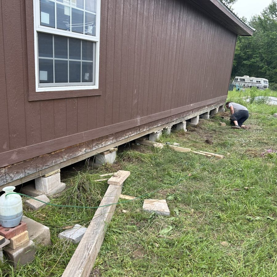 Technician inspecting and adjusting block piers under a manufactured home during leveling work in East Texas.